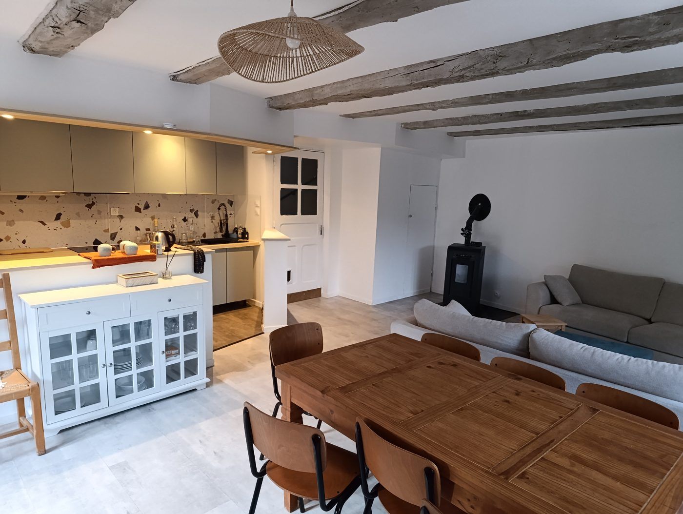 Pièce à vivre du bâtiment 2 : cuisine ouverte, grande table de repas, canapés et poêle sous les poutres